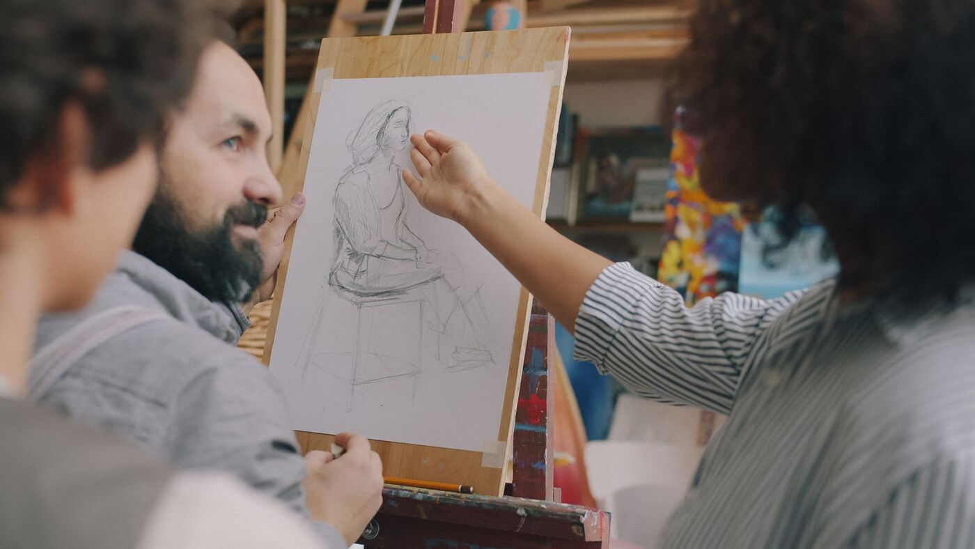 An instructor guiding a student's figure drawing at an easel